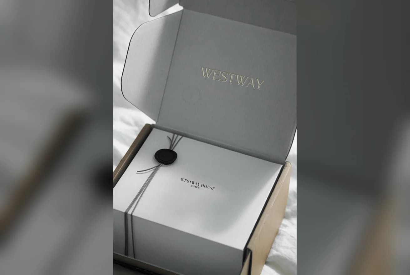 An open grey gift box with a wax seal and tissue paper
