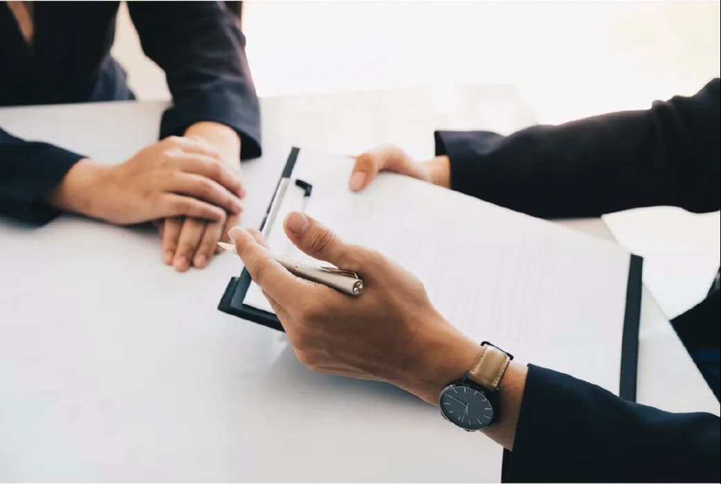 An interviewer with a clipboard across a white desk from a candidate