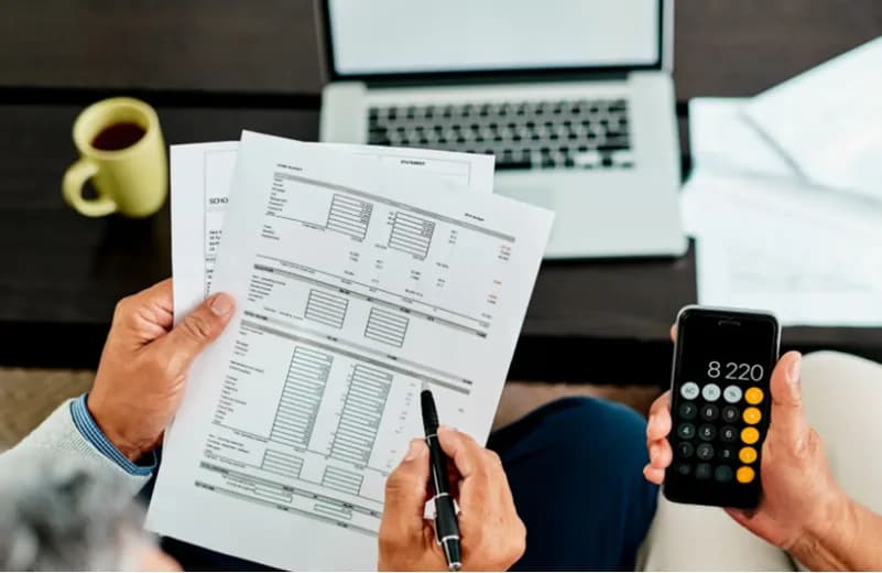 Hands holding a financial statement and a calculator on a phone