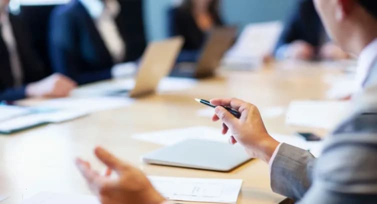 Colleagues around a meeting table, one holding a pen over papers