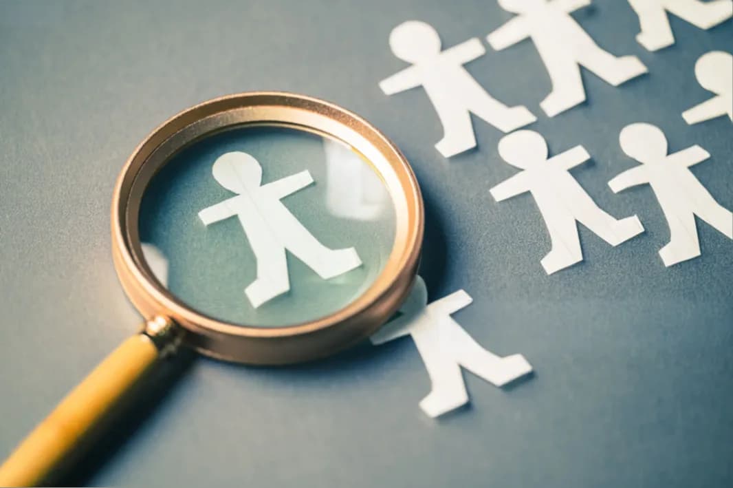 A magnifying glass over one paper figure among many