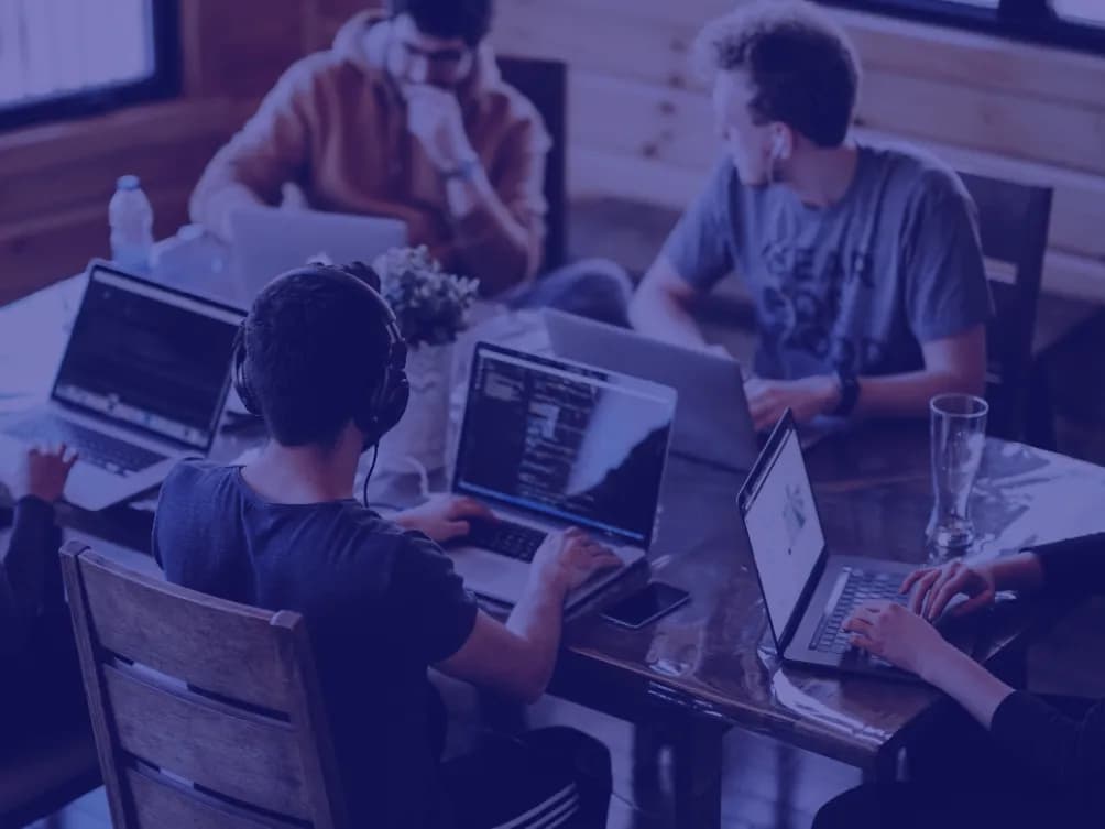 A team working on laptops around a table, tinted blue