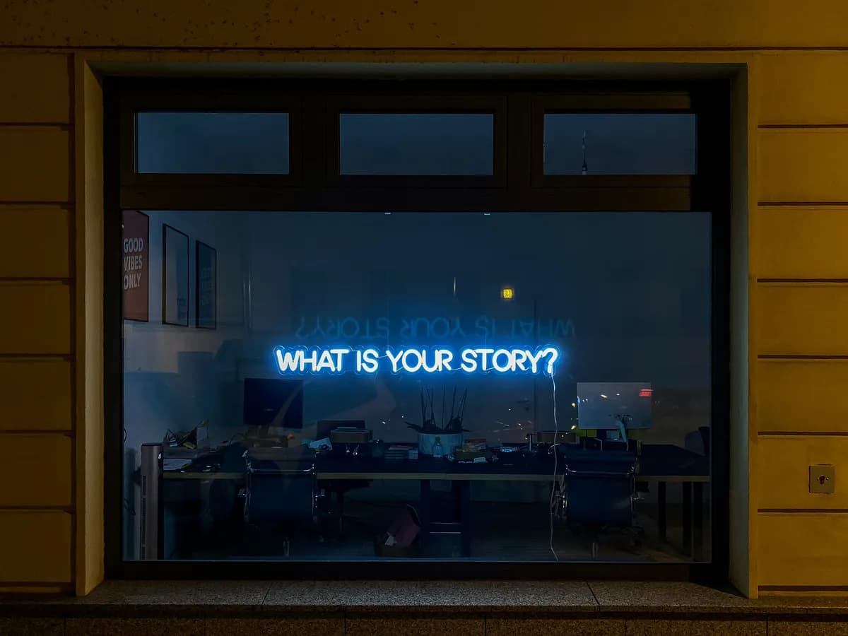 A neon sign asking What is your story? in a shop window