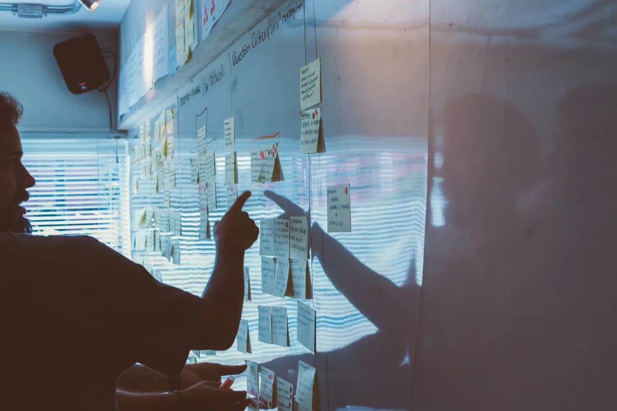 Two people pointing at notes pinned to a wall in a dim room