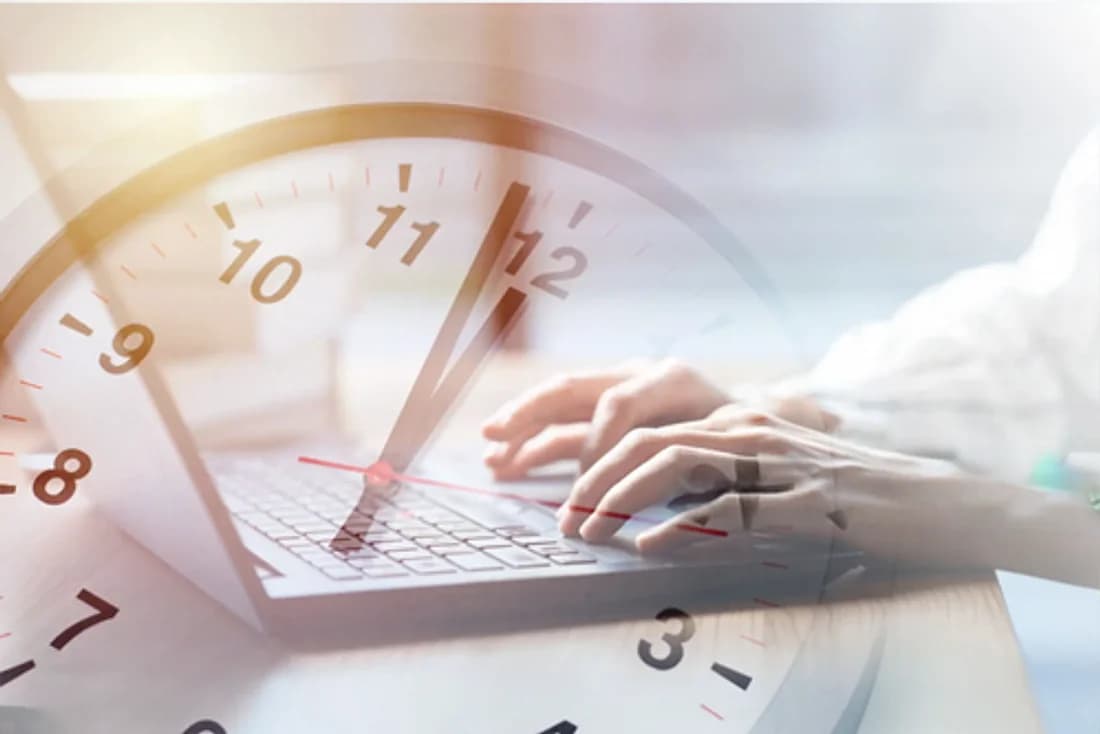 A clock face over hands typing on a laptop