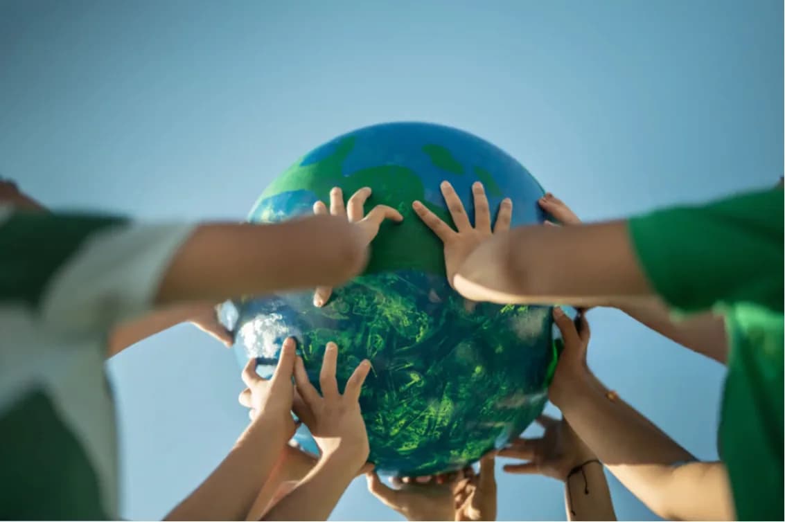Many hands holding up a globe against the sky