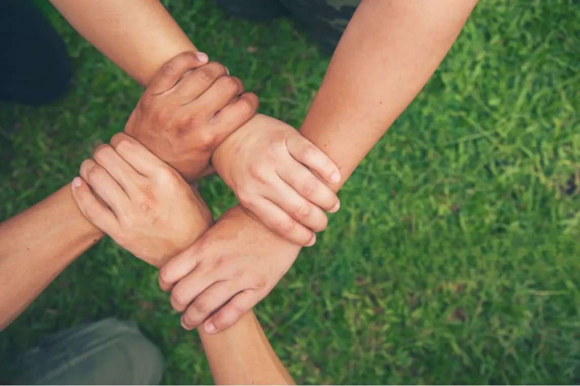 Hands linked at the wrists in a circle over grass